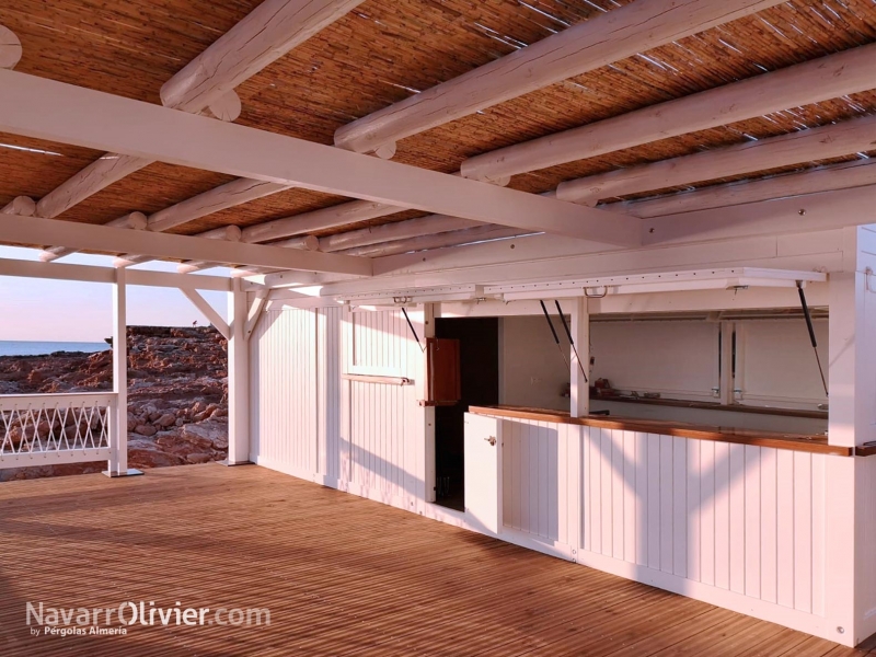 Chiringuito de madera sobre pilotes de madera con tarima y pérgola natural